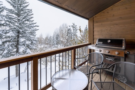 Snow-covered trees and a forest view from a cozy wooden balcony with a barbecue grill and patio furniture.