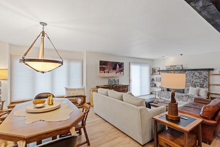 Wooden dining room table next to living room with beige couch, a brown leather couch, a television, and a fireplace