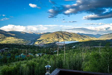 Scenic view of a mountainous landscape with a lake, town, and forested area under a partly cloudy sky during daylight.