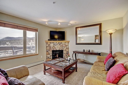 Living area offers a cozy fireplace, TV, 2 sofas, and a large window allowing ample natural light in.