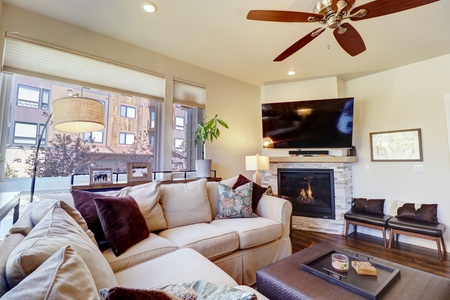 Cozy living room featuring large windows, a comfy sofa, fireplace, and large TV.