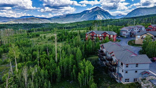 Aerial view of residential buildings surrounded by lush greenery with a mountainous landscape in the background.