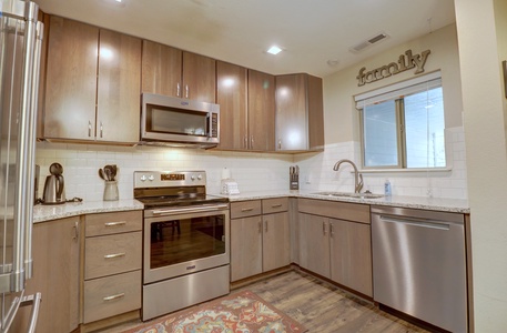 Modern kitchen with wooden cabinets, stainless steel appliances including a refrigerator, oven, microwave, and dishwasher, granite countertops, white subway tile backsplash, and a window above the sink.