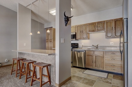 A kitchen and dining area featuring wooden cabinets, granite countertops, three bar stools, stainless steel appliances, and a decorative wall ornament.