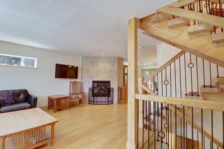 A living room featuring a mounted TV, wooden furniture, a tiled fireplace with a black metal guard, and an adjacent wooden staircase with metal railings.