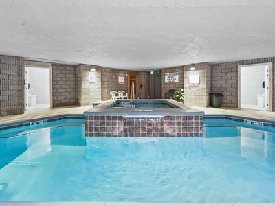 Indoor swimming pool area with a central hot tub. The pool has depth markers, and safety signage is visible above the hot tub area.