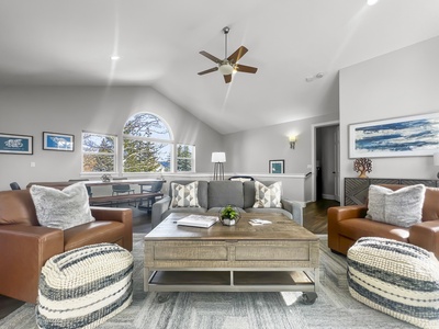 A modern living room with a gray sofa, two brown leather chairs, a wooden coffee table, and large windows letting in natural light. Neutral color palette with blue accents.