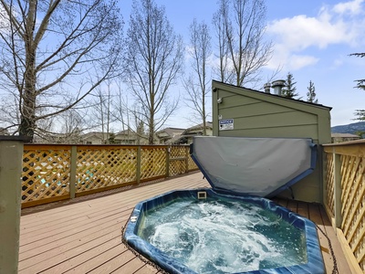 A rooftop hot tub with water jets active, surrounded by lattice fencing and bare trees, under a cloudy sky.