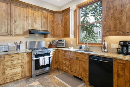 A spacious kitchen with wooden cabinets, stainless steel appliances, a large window, and granite countertops.