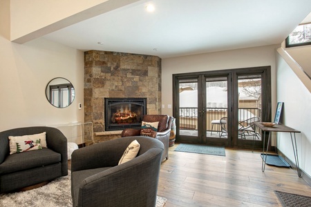 A cozy living room featuring armchairs, a fireplace with a stone surround, and French doors leading to a snow-covered outdoor area.