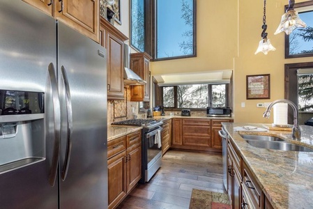 Spacious modern kitchen with stainless steel appliances, wooden cabinets, large windows, granite countertops, double sink, and pendant lighting.