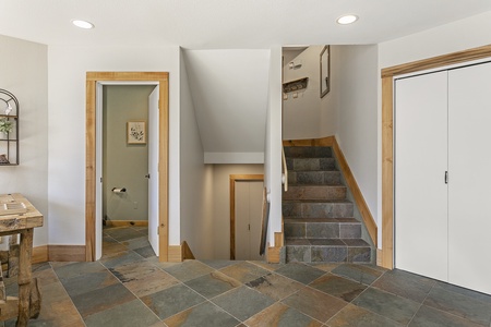 A tiled hallway features a closed closet door, an open bathroom door, and a staircase leading up and down.