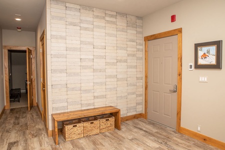 A hallway with a beige door, stone brick accent wall, wooden bench with three wicker baskets underneath, and a framed picture on the wall.