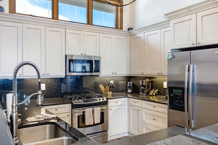 A modern kitchen with white cabinetry, stainless steel appliances, granite countertops, a double sink with a spring faucet, and a microwave mounted above the gas range.