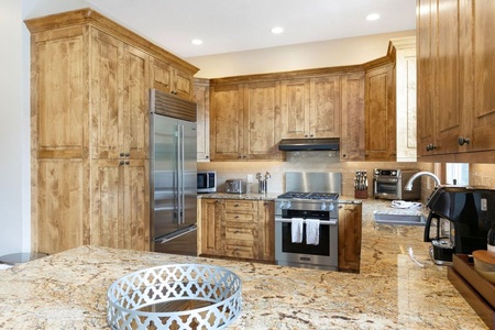 A modern kitchen with wooden cabinets, granite countertops, stainless steel appliances, and a circular decorative tray on the island.