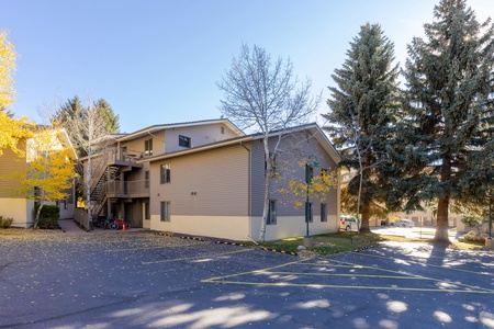 A two-story apartment building with outside staircases, surrounded by trees and a parking area. .