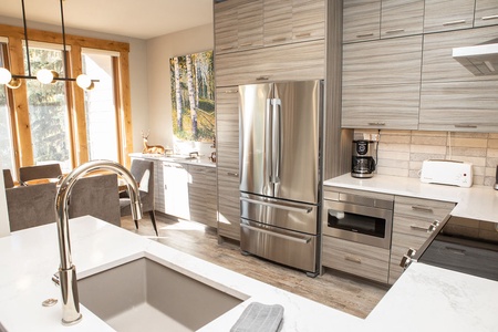 Modern kitchen with light wood cabinets, stainless steel appliances, white countertops, sink island, and dining area with large windows.