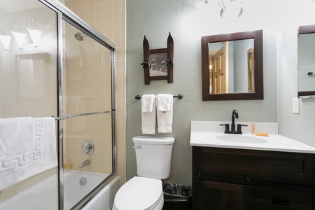 Bathroom with a glass-enclosed tub, toilet with white towels above, a dark wood vanity, and a mirror.