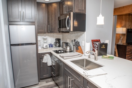 A modern kitchen featuring stainless steel appliances, dark wood cabinets, a white marble countertop with a sink, and various small kitchen appliances and utensils neatly arranged.