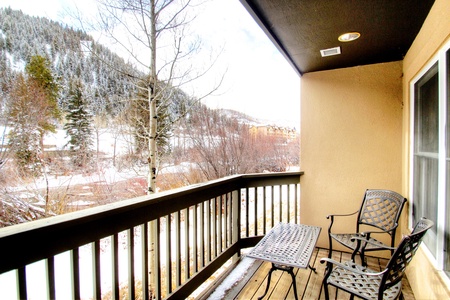 A small balcony overlooking a snowy landscape with two metal chairs and a table.