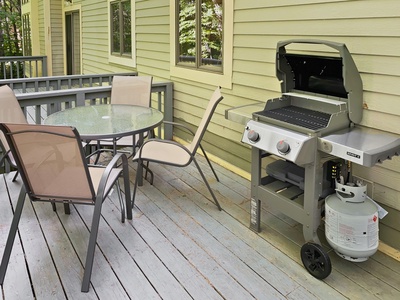 A patio with a round glass table and four chairs next to a barbecue grill.