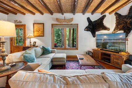 - Rustic living room with wood beams and forest views through wide windows   - Comfortable sectional sofa ideal for family movie nights or relaxation   - Mountain cabin style decor blends charm with modern entertainment setup