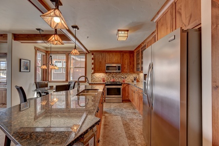 Modern kitchen with wooden cabinets, granite countertops, stainless steel appliances, and pendant lighting above the island.