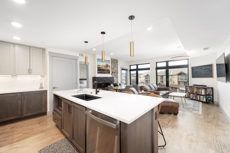 Modern open-concept kitchen and living room with wooden floors, a marble countertop island, modern pendant lights, and large windows letting in natural light