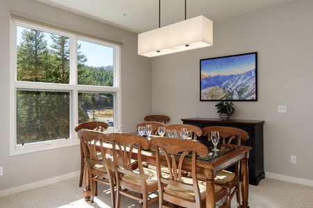 A dining room with a wooden table set for six, with lovely views out the large windows