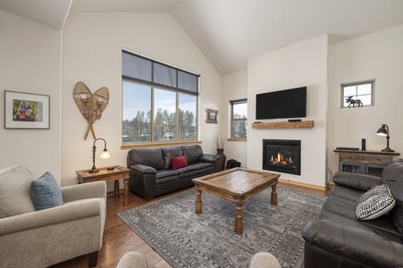 Spacious living area with a gas fireplace, a wall-mounted TV, and large windows bathing the space in natural light