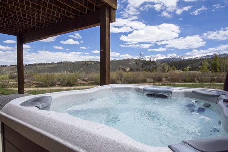 A private hot tub under a wooden pergola overlooks a scenic landscape