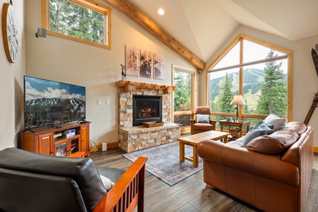 Living room with stone fireplace and tall windows framing peaks   - Cozy seating and natural wood accents for mountain comfort   - Gather for movies, games, or fireside relaxation after activities