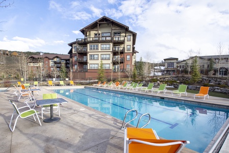 Outdoor swimming pool with colorful lounge chairs and tables and chairs, set in front of a beautiful landscape of mountains.