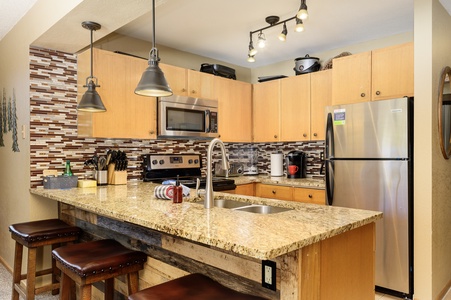 Modern kitchen with granite counter tops, wooden cabinetry, stainless steel appliances, and a tiled backsplash, with pendant lighting.