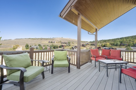 A wooden deck with cushioned chairs, a covered area, and views of a hilly landscape.