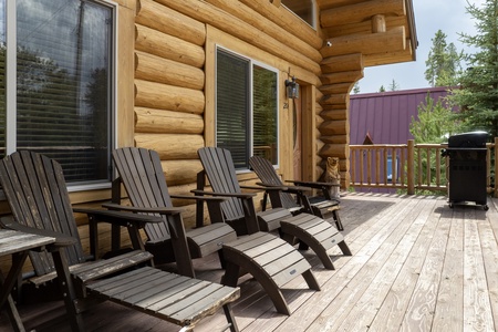 A wooden deck with several dark Adirondack chairs for soaking up sunshine or stargazing