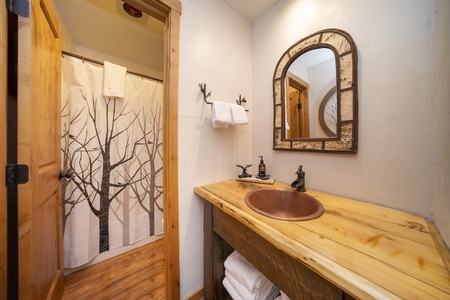 An updated bathroom with a wooden countertop, copper sink, mirror,  with a shower/tub combo