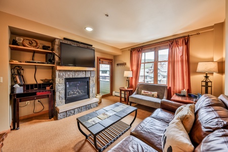 Cozy Living Area with wall mounted TV above a cozy gas fireplace with windows overlooking the village of Winter Park Resort