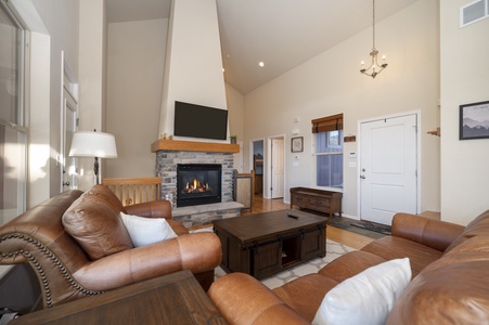 A cozy living room with leather sofas, high ceilings, the room is bathed in natural light from the large windows