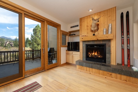 A cozy living room with a fireplace, TV, and  sliding glass doors with views of nature outside