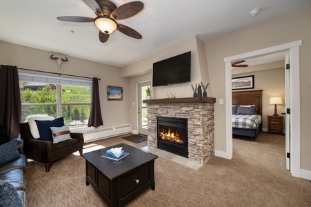 A cozy living room with a stone fireplace, wall mounted TV , ceiling fans for your comfort