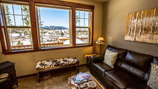 A cozy, sunlit living room with a window framing a mountain landscape.