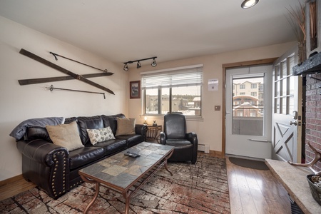 A cozy living room with a black leather sofa, a recliner, a coffee table,  and a large window allowing the natural light into the home