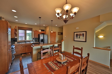 A cozy kitchen and dining area with wooden furniture, stainless steel appliances, and a chandelier above the dining table.