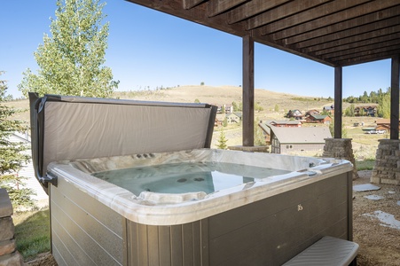 An outdoor private hot tub is situated under a wooden pergola, overlooking a scenic landscape