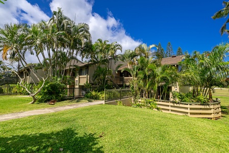 A tropical Hawaiian-style building surrounded by lush palm trees and manicured lawns, framed by brilliant blue skies and fluffy white clouds.