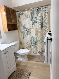 Step into your private bathroom with a fresh botanical-print shower curtain, warm wood-look flooring, and a clean, modern vanity. Your towels and essentials are close at hand, making it easy to settle in.