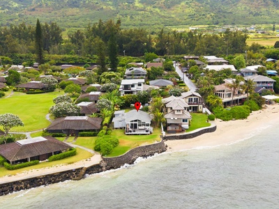 Aerial view of a beachfront neighborhood with residential homes nestled between lush mountains and calm coastal waters, showcasing the property's scenic island location.