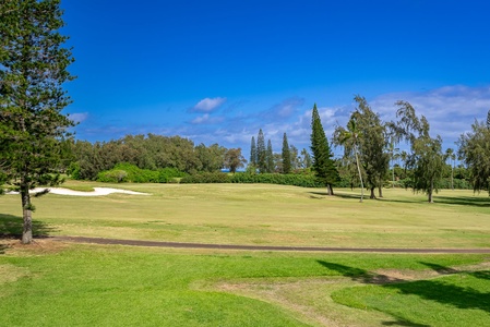 A pristine golf course with manicured greens and fairways surrounded by mature trees and blue skies, located near the property.
