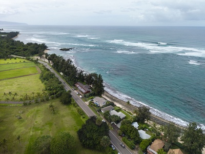 Stunning aerial perspective shows pristine coastline with turquoise waters, lush tropical landscape, and charming beachfront properties creating an idyllic island paradise setting.